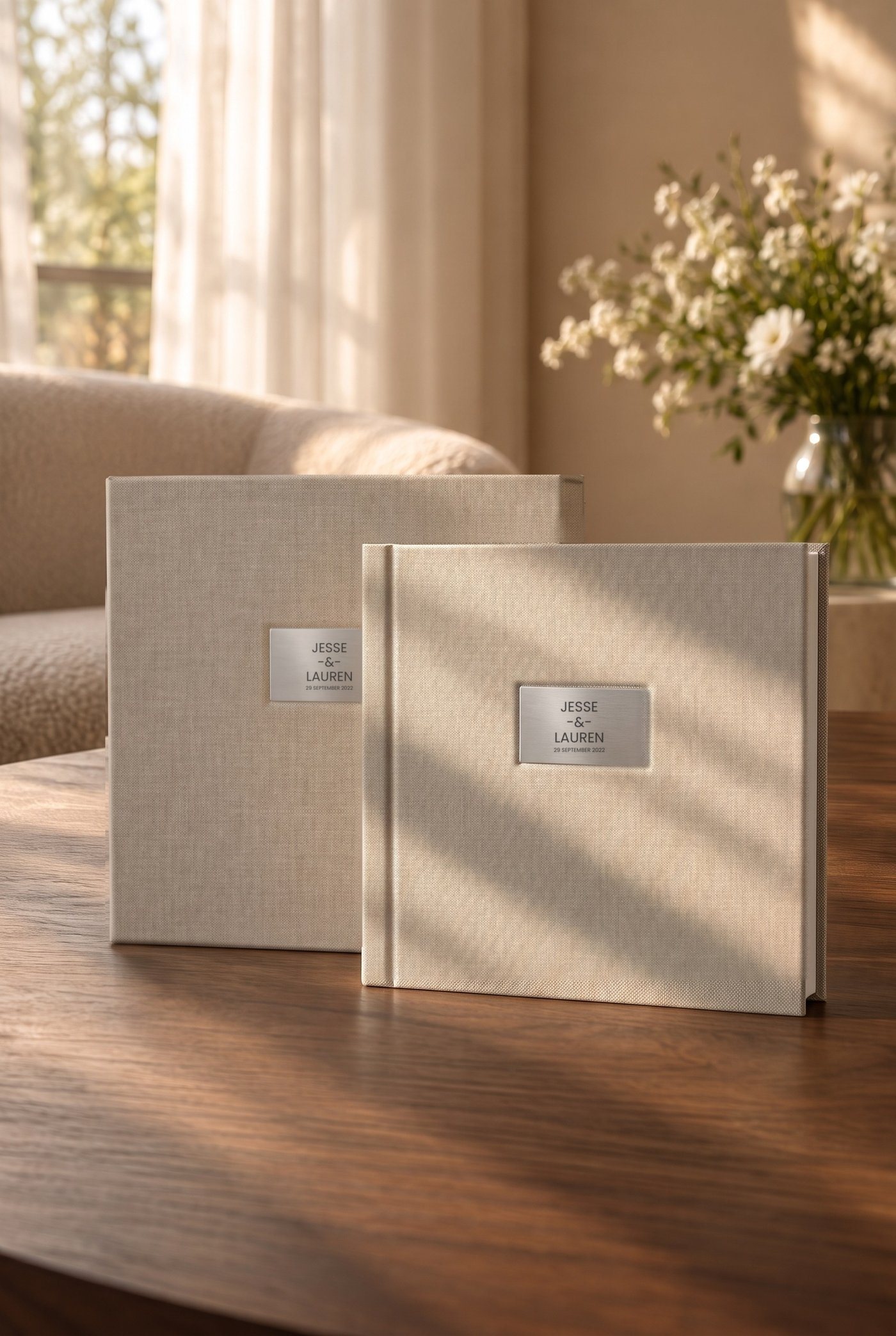 A natural linen album and its keepsake box with engraved plates, standing on a walnut table in afternoon sun